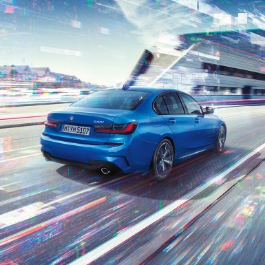BMW 3 Serisi Sedan, arka yandan görünüm. BMW 3 Serisi Sedan’ın şehir manzarası önünde gündüz arkadan görünümü.