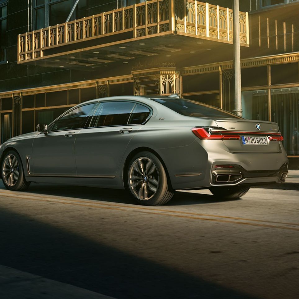 V12 motor ile BMW M760Li xDrive Sedan BMW M760Li xDrive Sedan, şehir içinde gökdelenlerin önünde, arka yandan görünüm.