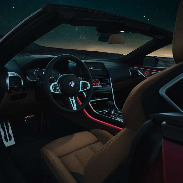 BMW M8 Competition Cabrio, kokpit. BMW M8 Competition Cabrio, M deri direksiyon ve kırmızı ortam aydınlatmasıyla kokpitin gece görünümü.