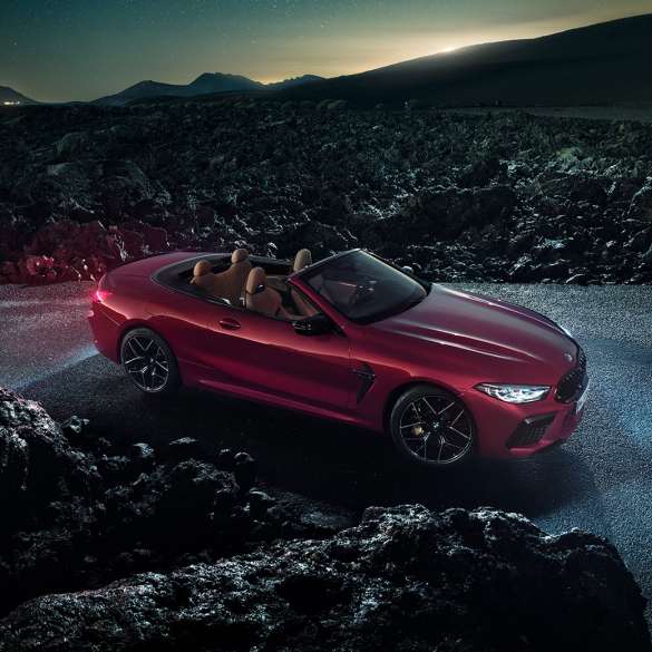 BMW M8 Competition Cabrio, yandan görünüm. Metalik Kırmızı/Motegi BMW M8 Competition Cabrio açık softtop ile gece asfalt üzerinde yandan görünüm.