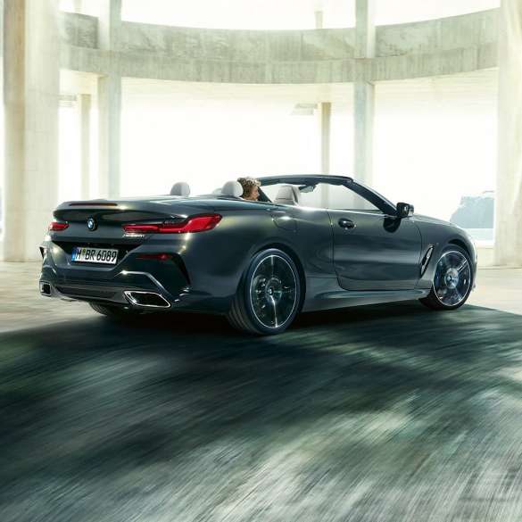 BMW M850i xDrive Cabrio, arkadan görünüm. Açık softtop ile metalik Gri/Dravit BMW M850i xDrive, beton bina yanından geçerken, arkadan görünüm.