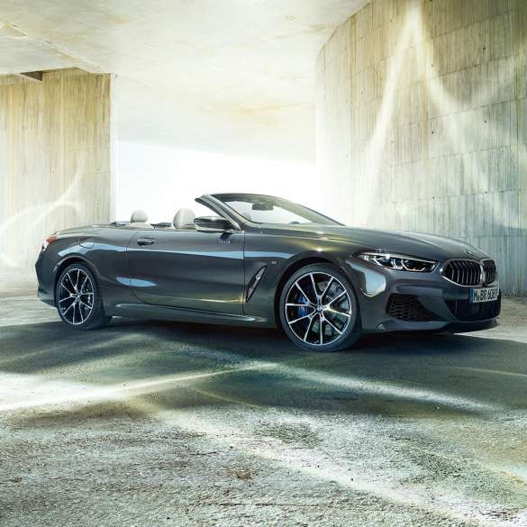 BMW M850i xDrive Cabrio, yandan görünüm. Açık softtop ile Metalik Gri/Dravit BMW M850i xDrive Cabrio, beton bina önünde, yandan görünüm.
