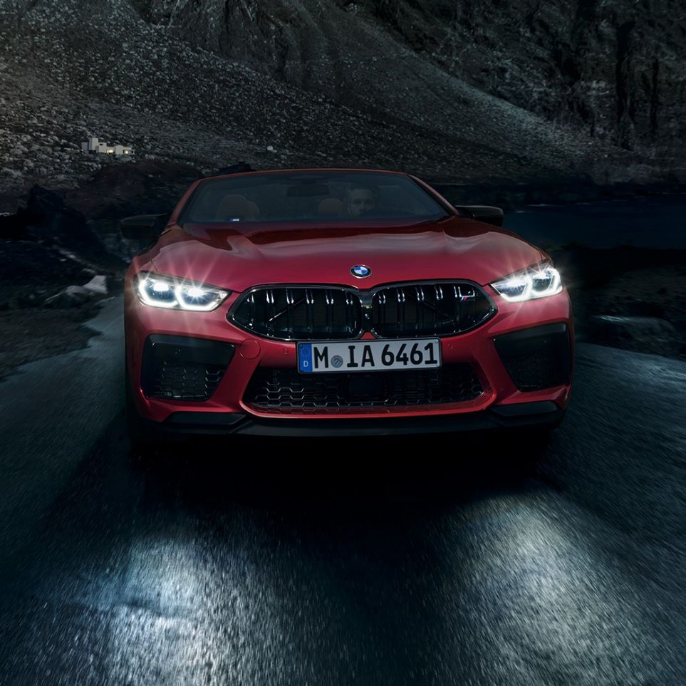 BMW M8 Competition Cabrio, önden görünüm. Gece sürüşü sırasında parlayan farlarıyla metalik Kırmızı/Motegi BMW M8 Competition Cabrio, önden görünüm.