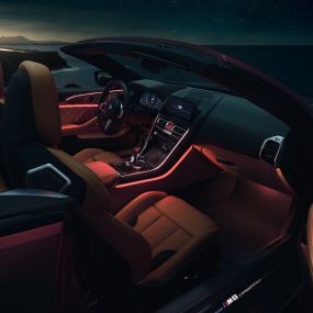 BMW M8 Competition Cabrio, iç tasarım. Gece kırmızı ortam aydınlatmasıyla, açık softtop ile BMW M8 Competition Cabrio’nun iç tasarımı.