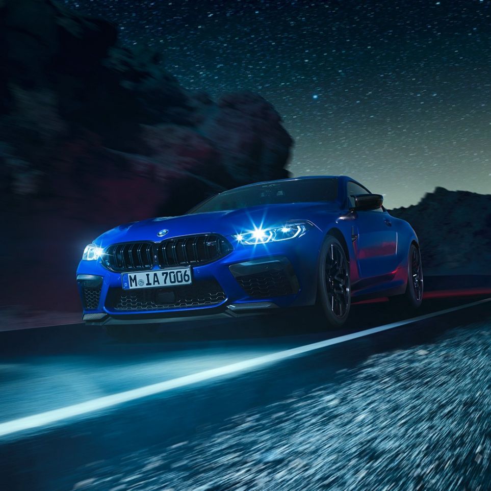 BMW M8 Competition Coupé sürüş sırasında, önden görünüm. Parlak LED farlarıyla gece sürüşü sırasında Metalik Mavi/Marina Bay BMW M8 Competition Coupé, önden görünüm.