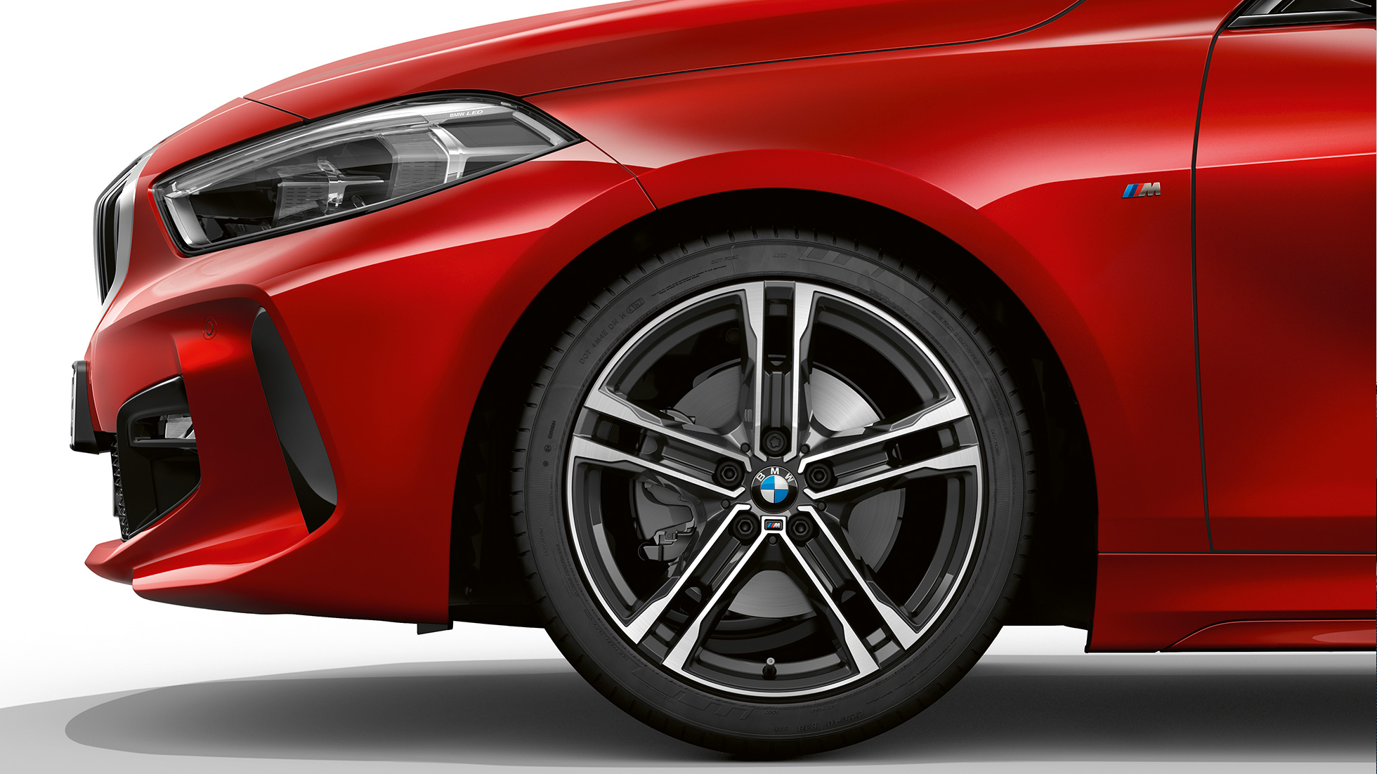 BMW 1 Serisi M Sport Modeli, ön tasarımın yandan görünümü. BMW 1 Serisi Metalik Kırmızı/Melbourne M Sport Modeli, 17 inç, Çift kollu, stil 550 M, bicolor M hafif alaşım jantlar ile ön tasarımın yandan görünümü.
