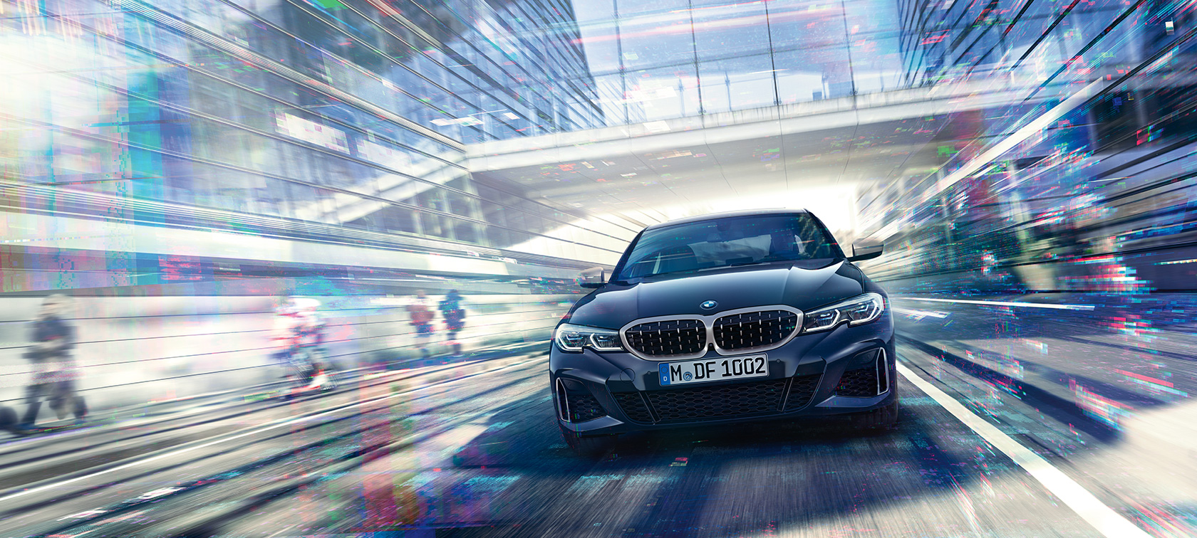 Yeni BMW 3 Serisi Sedan, BMW M340i xDrive’ın önden görünümü. Şehir içinde camlı binalar arasında sürüş sırasında BMW M340i xDrive Sedan’ın önden görünümü.