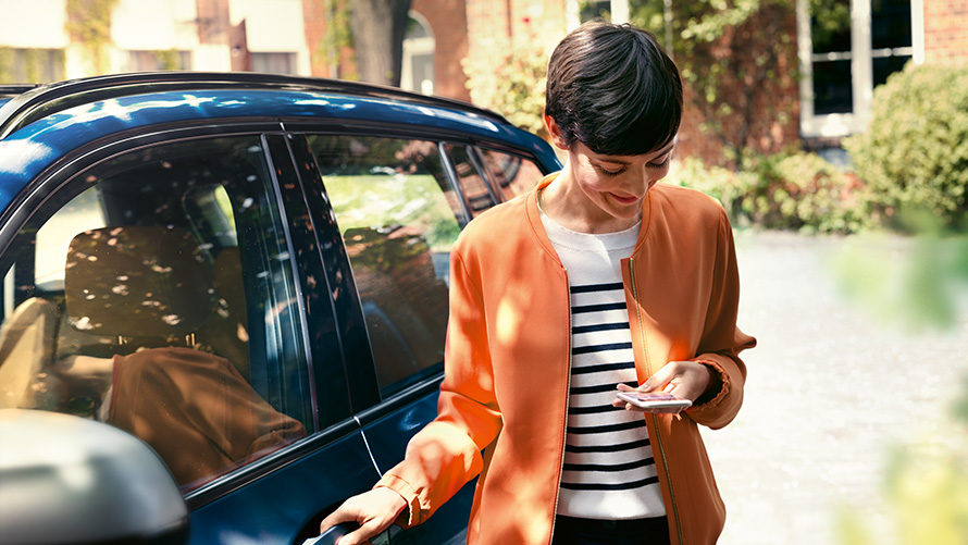 BMW Servis, elinde akıllı telefonu ile BMW'sinin kapısının yanında duran kadın BMW Servis, elinde akıllı telefonu ile BMW'sinin kapısının yanında duran kadın