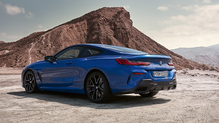 Çapraz arkadan görünüm BMW 8 Serisi Coupé M Sport G15 LCI BMW 8 Serisi Coupé M Sport G15 LCI Metalik Mavi/M Portimao Kayaların önünde dururken çapraz arkadan görünüm
