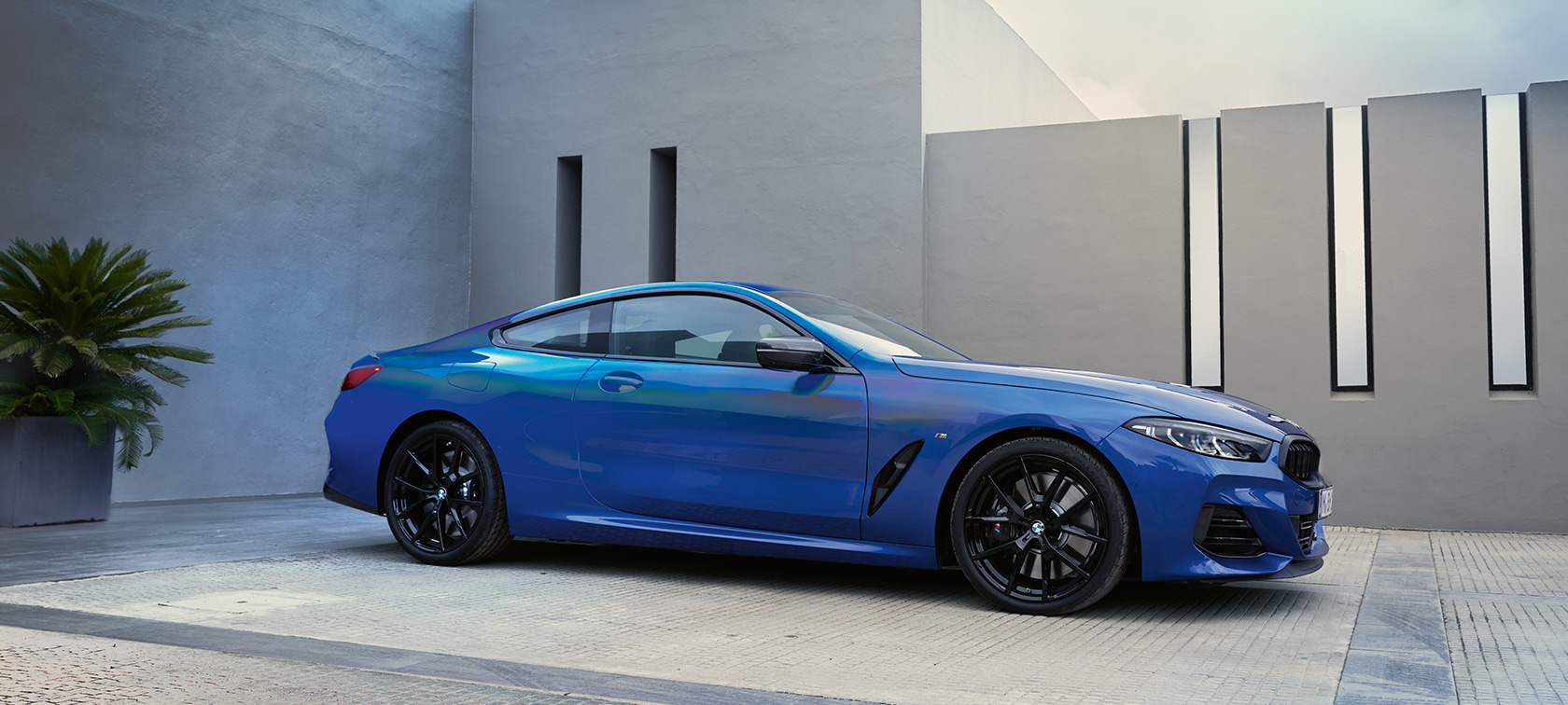 BMW 8 Serisi Coupé G15 LCI Metalik Mavi/M Portimao Bir evin duvarı önünde dururken yandan görünüm