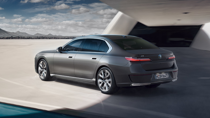 BMW i7 Sedan G70, BMW Individual Metalik Gri/Oxid, bina önünde hareketsiz halde arka çaprazdan görünüm BMW i7 Sedan donanımı, arka çaprazdan görünüm