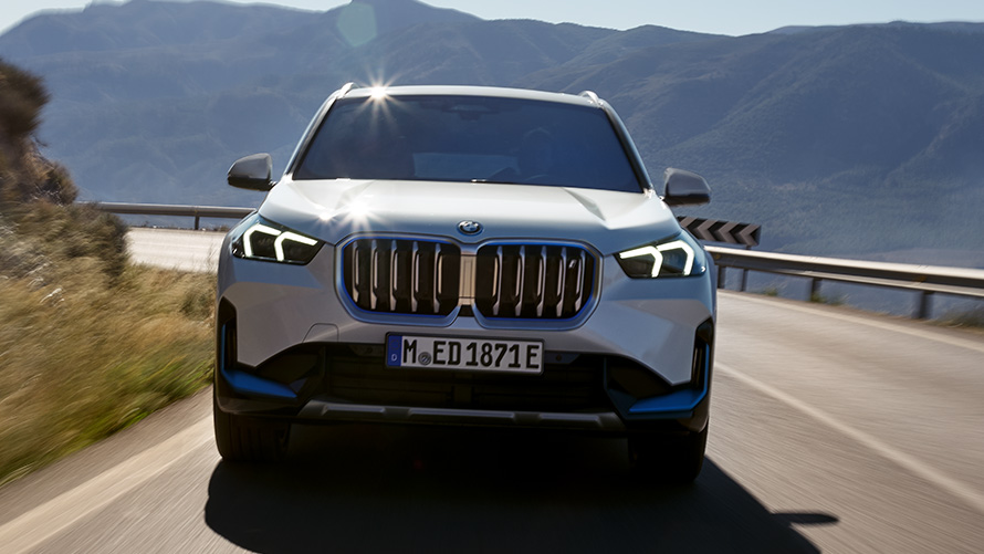 BMW iX1 U11 BEV, Önden görünüm BMW iX1 U11 BEV, Metalik Beyaz/Mineral, Dağ yolunda sürüş sırasında önden görünüm