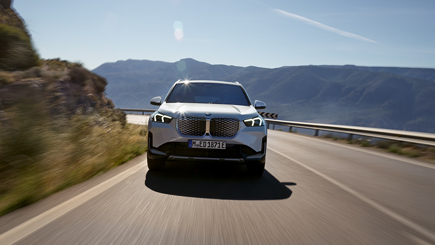 BMW iX1 U11 BEV, Önden görünüm BMW iX1 U11 BEV, Metalik Beyaz/Mineral, Dağ yolunda sürüş sırasında önden görünüm
