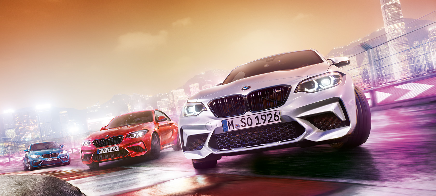 Yeni BMW M2 Competition hareket halinde Üç adet Yeni BMW M2 Competition otomobil gece şehir manzarası önünde yarış pistinde drift yapıyor.