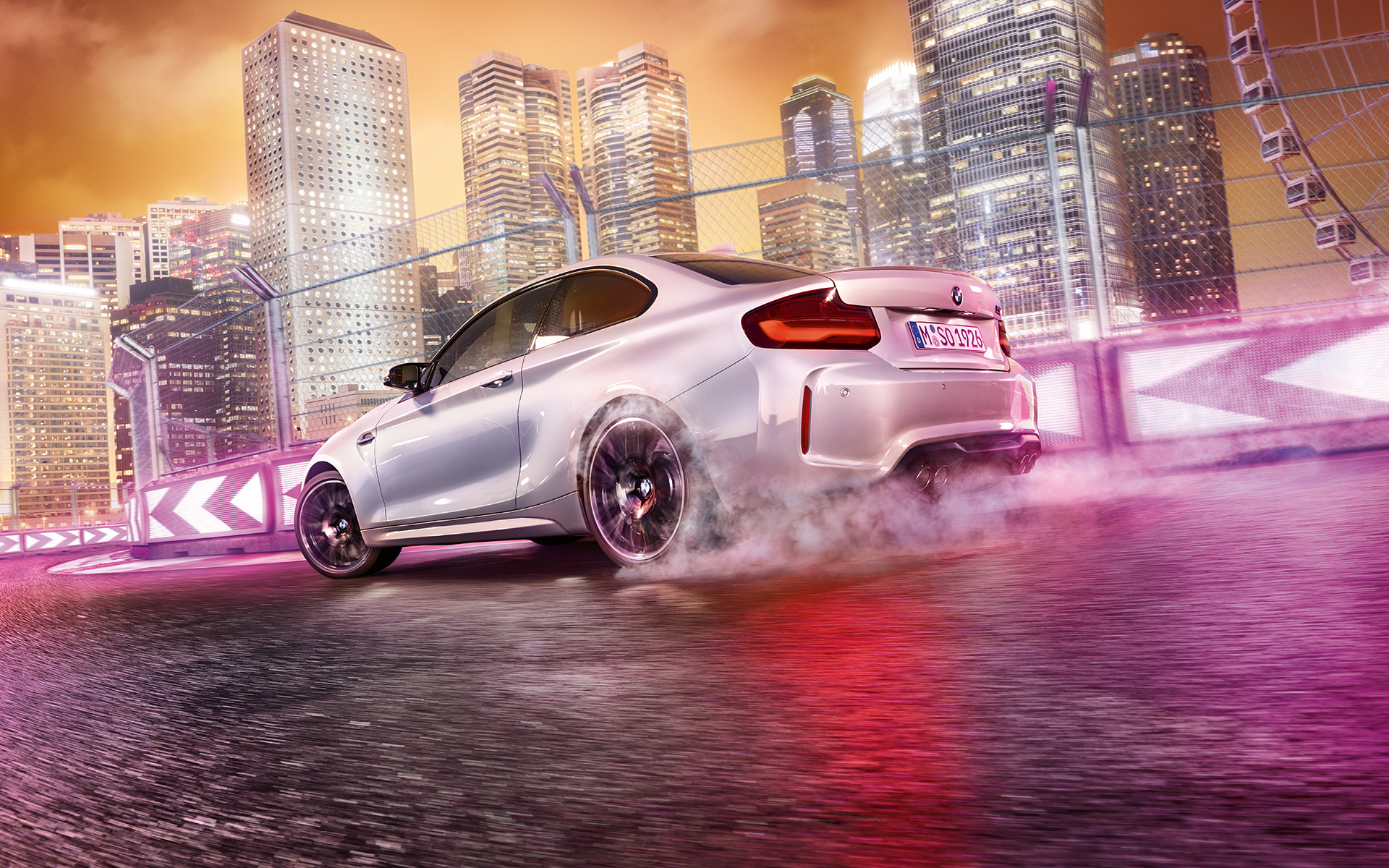 Yeni BMW M2 Competition hızlanıyor Beyaz renkte Yeni BMW M2 Competition gece şehir manzarası önünde yarış pistinde drift yapıyor.