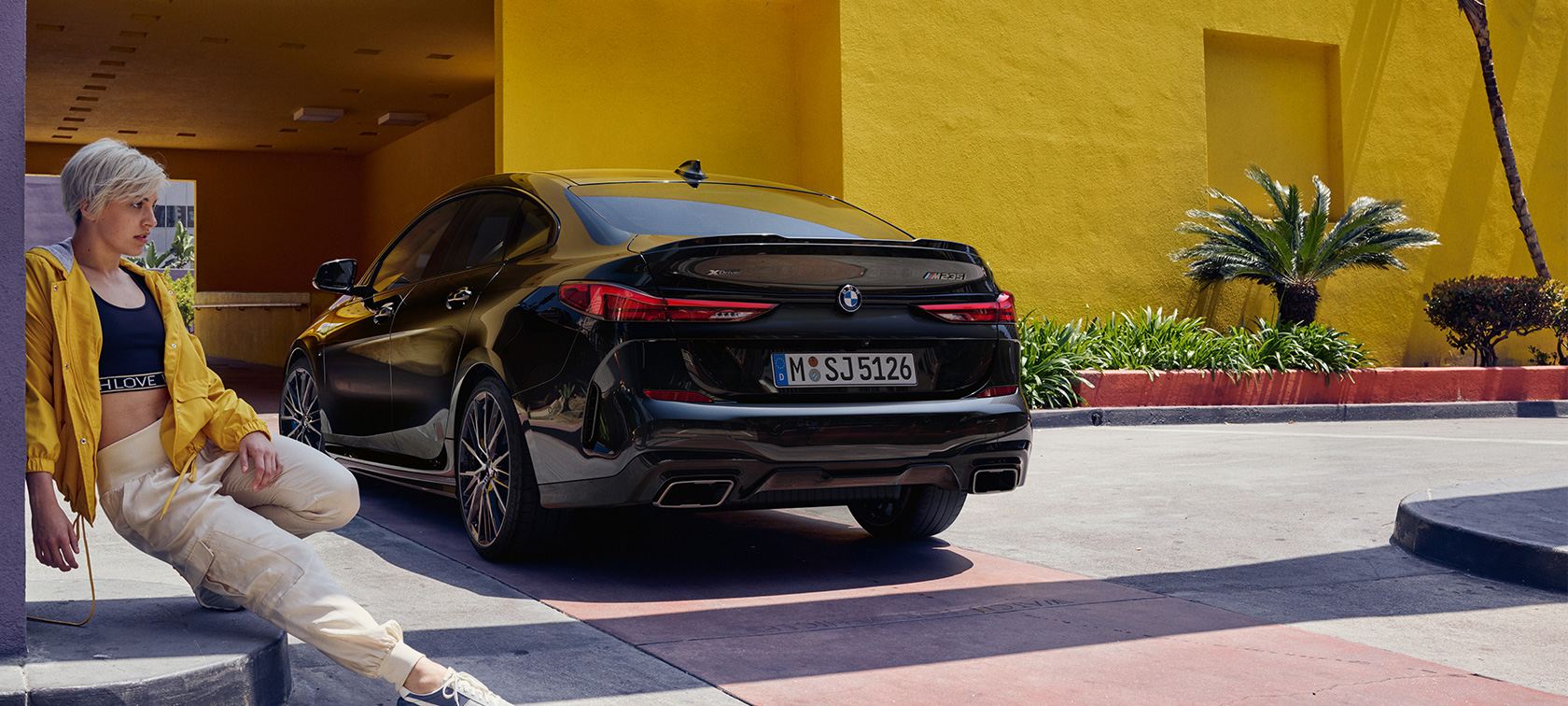 BMW M235i xDrive Gran Coupé arkadan görünüm BMW M235i xDrive Gran Coupé Metalik Siyah/Sapphire F44 önde kadın ile birlikte arkadan görünüm