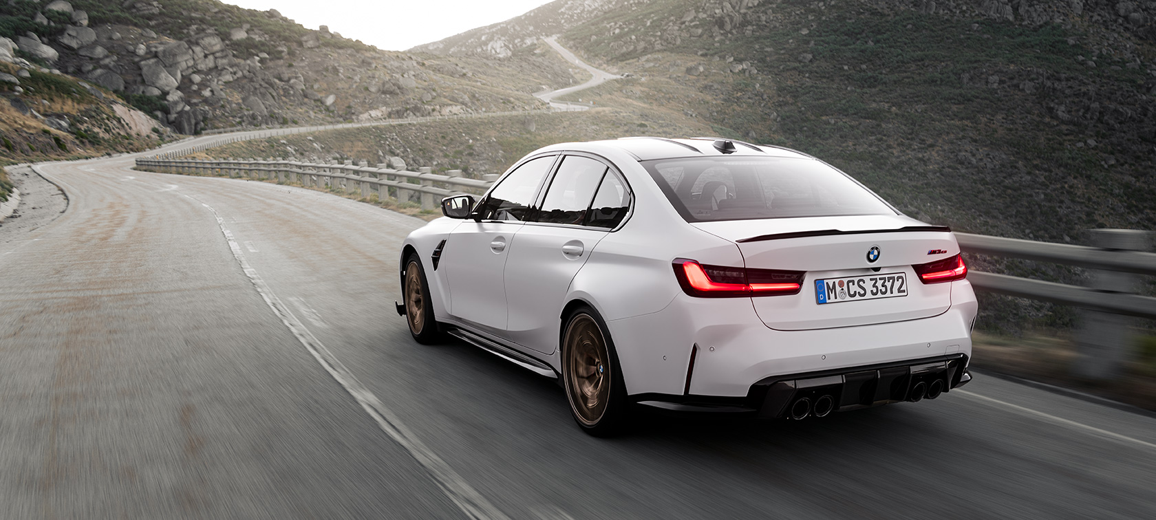 BMW M3 CS G80, sürüş esnasında arka çaprazdan görünüm BMW M3 CS G80, dağlık yolda sürüş esnasında arka çaprazdan görünüm