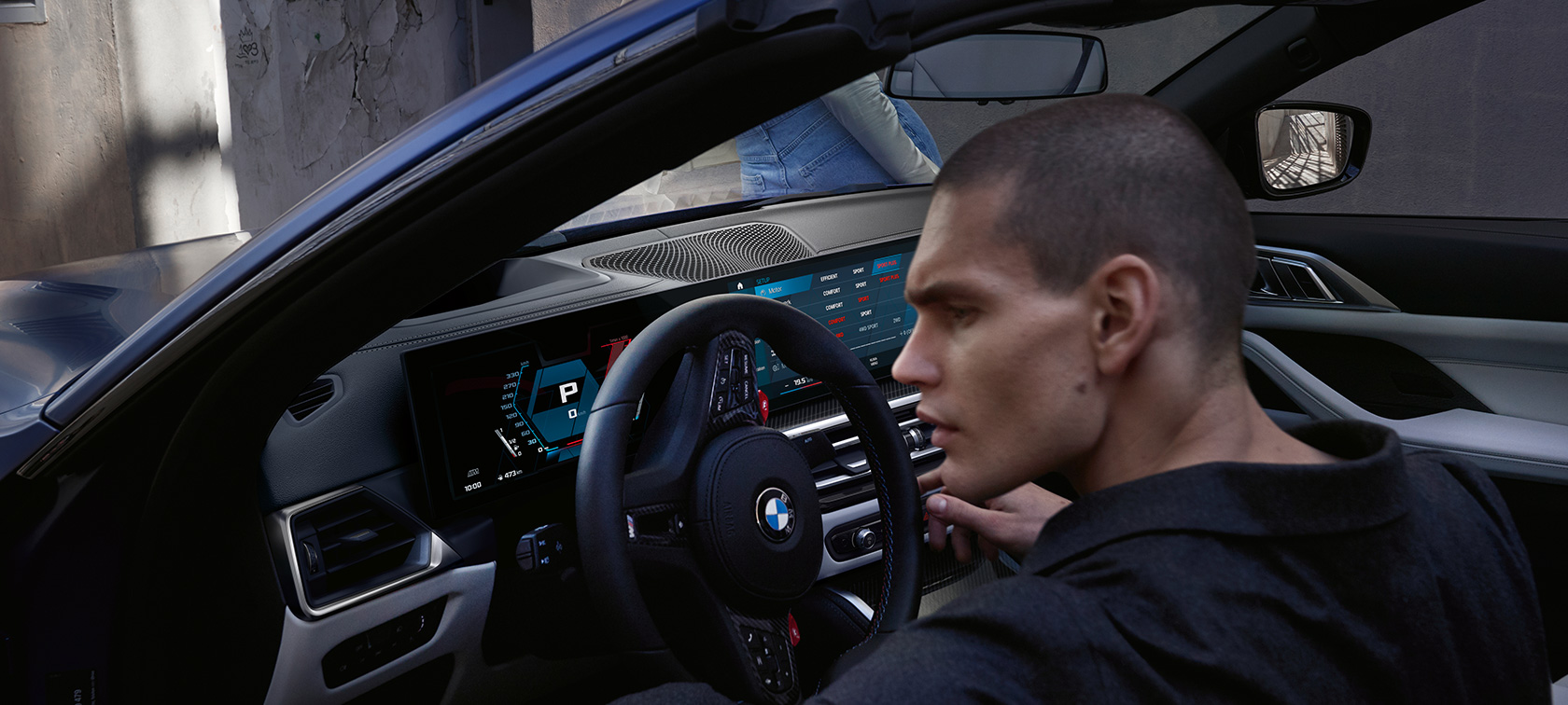 M xDrive özellikli BMW M4 Competition Cabrio G83, kokpit M xDrive özellikli BMW M4 Competition Cabrio G83, BMW Individual Metalik Mat Mavi/Portimao, erkek modelle birlikte kapı açık halde kokpit görüntüsü