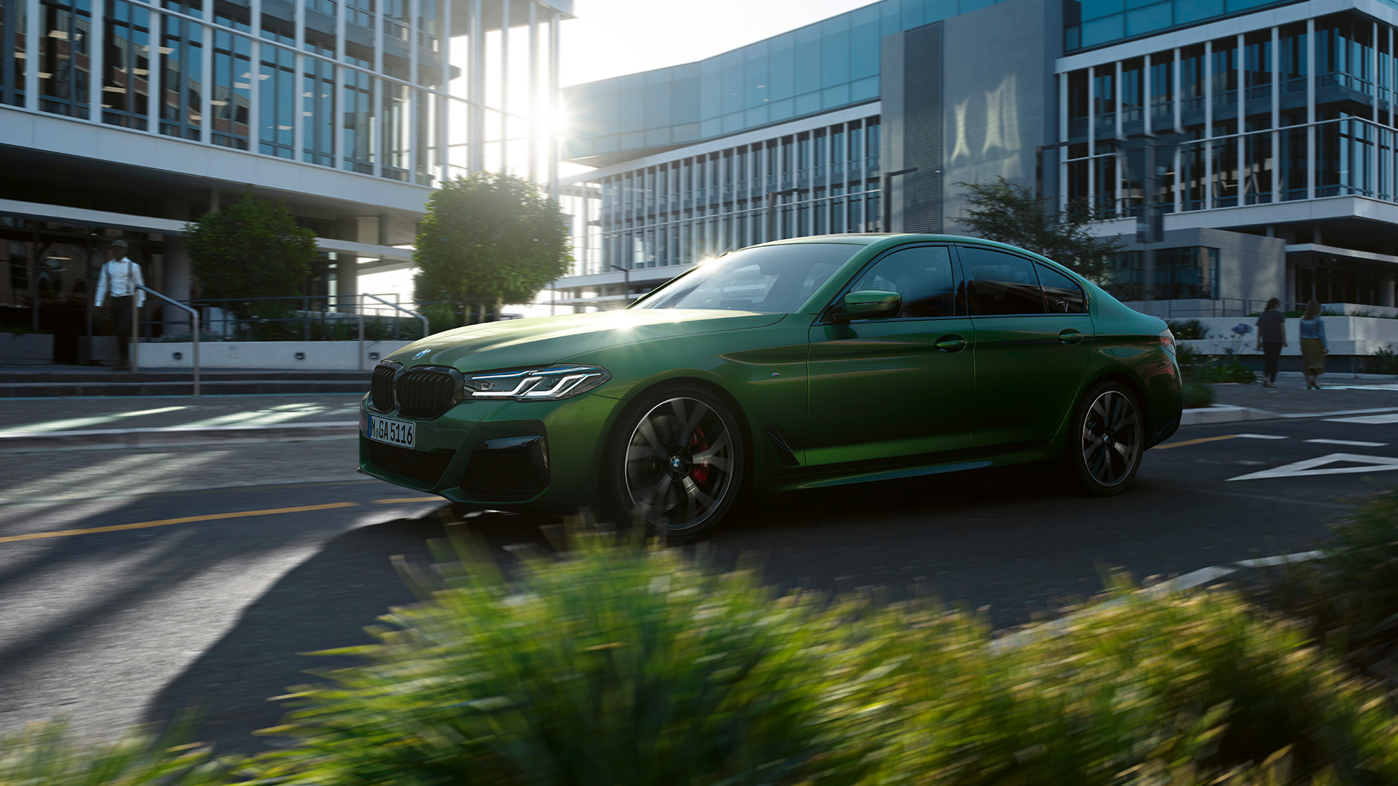 BMW M550i xDrive Sedan G30 LCI sürüş sırasında yandan görünüm BMW M550i xDrive Sedan G30 LCI BMW Individual Metalik Yeşil/Verde Ermes şehir içinde sürüş sırasında yandan görünüm