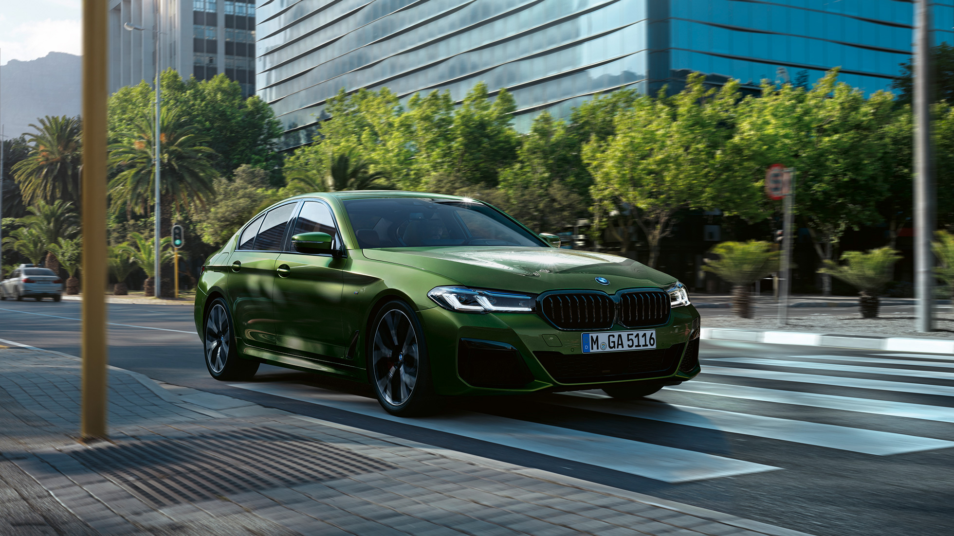 BMW M550i xDrive Sedan G30 LCI sürüş sırasında önden görünüm BMW M550i xDrive Sedan G30 LCI BMW Individual Metalik Yeşil/Verde Ermes şehir içinde sürüş sırasında önden görünüm
