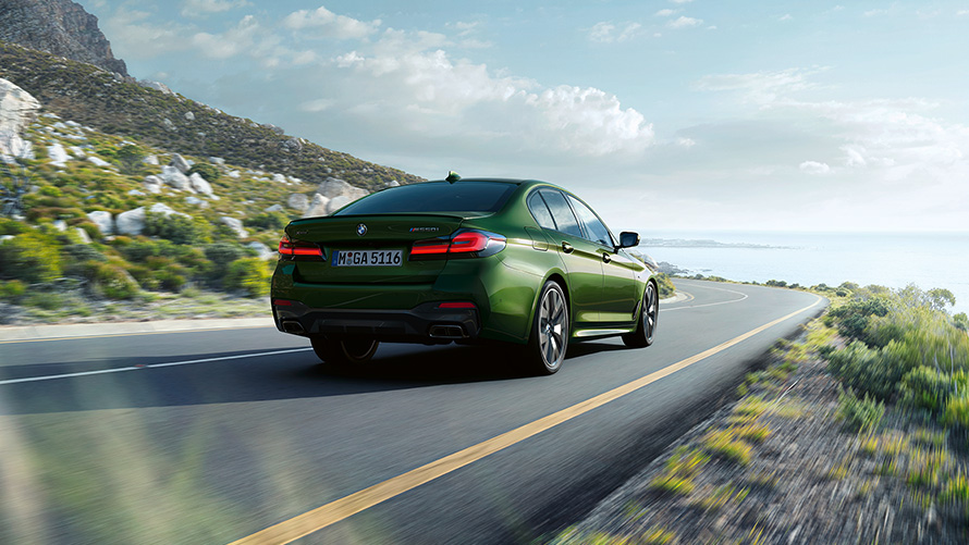 BMW M550i xDrive Sedan G30 LCI BMW Individual Metalik Yeşil/Verde Ermes sürüş sırasında arka çaprazdan görünüm