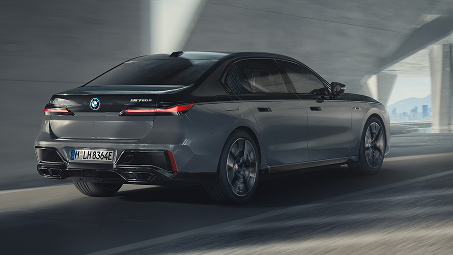 BMW M760e xDrive Sedan G70 M Performance BMW M760e xDrive Sedan G70 M Performance, BMW Individual Metalik Siyah/Sapphire BMW Individual Metalik Gri/Dravite iki tonlu gövde rengi, yolda sürüş sırasında arka çaprazdan görünüm