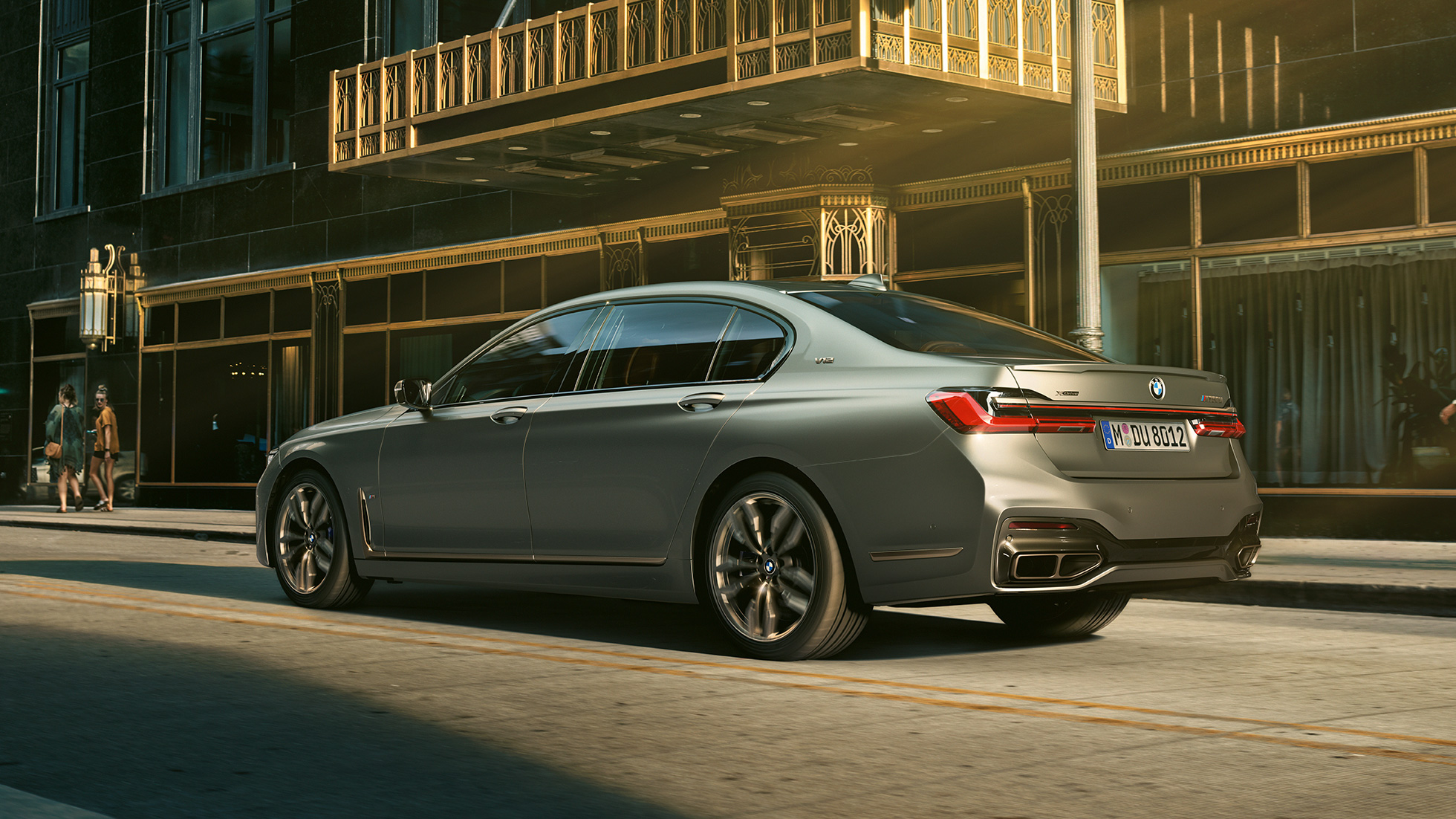 V12 motor ile BMW M760Li xDrive Sedan BMW M760Li xDrive Sedan, şehir içinde gökdelenlerin önünde, arka yandan görünüm.