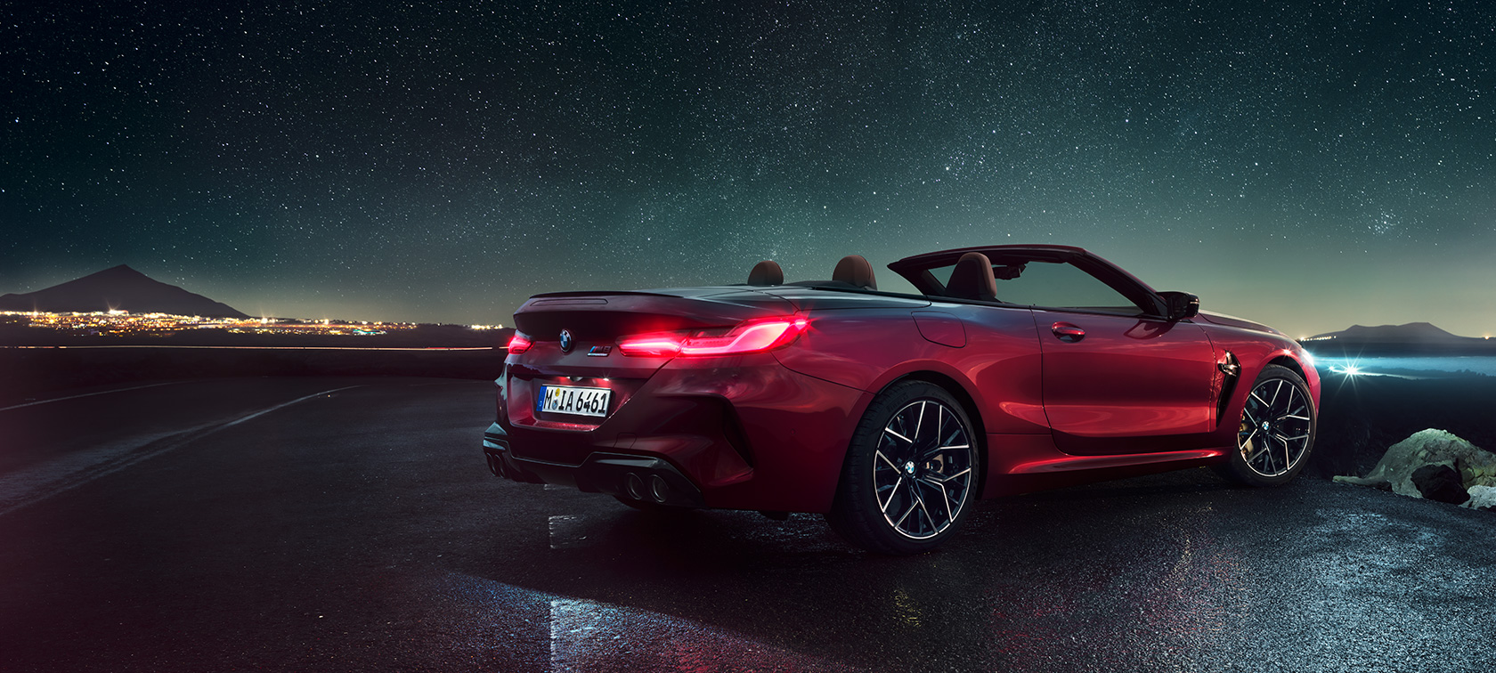 BMW M8 Competition Cabrio, arkadan görünüm. Açık softtop ile Metalik Kırmızı/Motegi BMW M8 Competition Cabrio, yıldızlı gökyüzü altında arkadan görünüm.