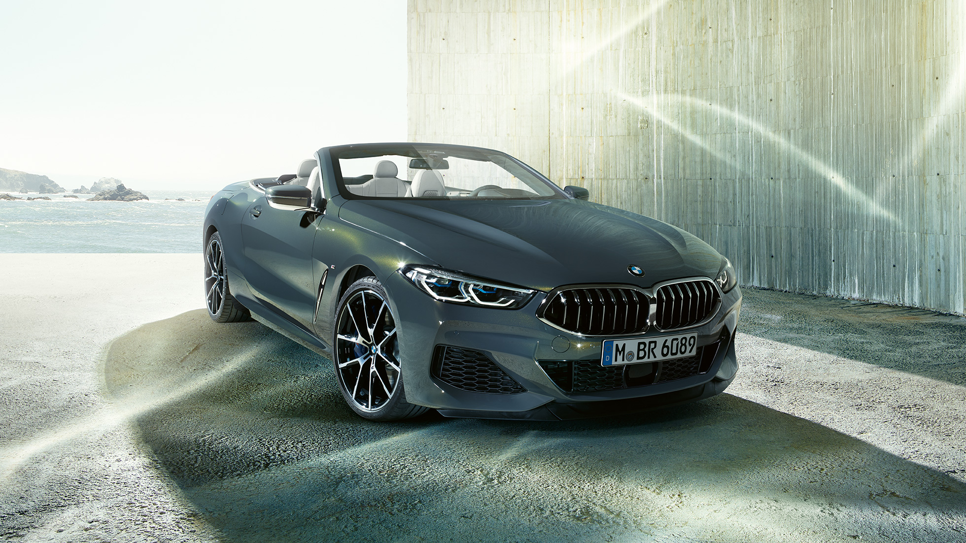 BMW M850i xDrive Cabrio, önden görünüm. Açık softtop ile Metalik Gri/Dravit BMW M850i xDrive Cabrio, sahilde önden görünüm.