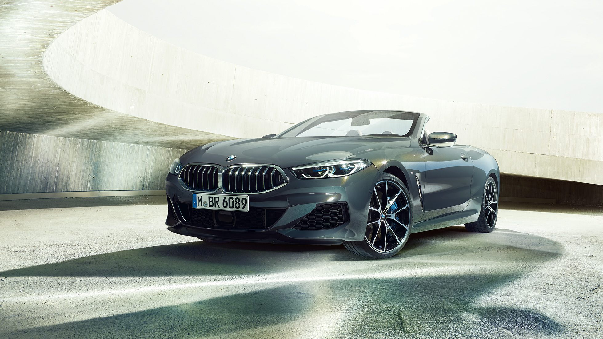 BMW M850i xDrive Cabrio, önden görünüm. Açık softtop ile Metalik Gri/Dravit BMW M850i xDrive Cabrio, beton bina içinde, önden görünüm.