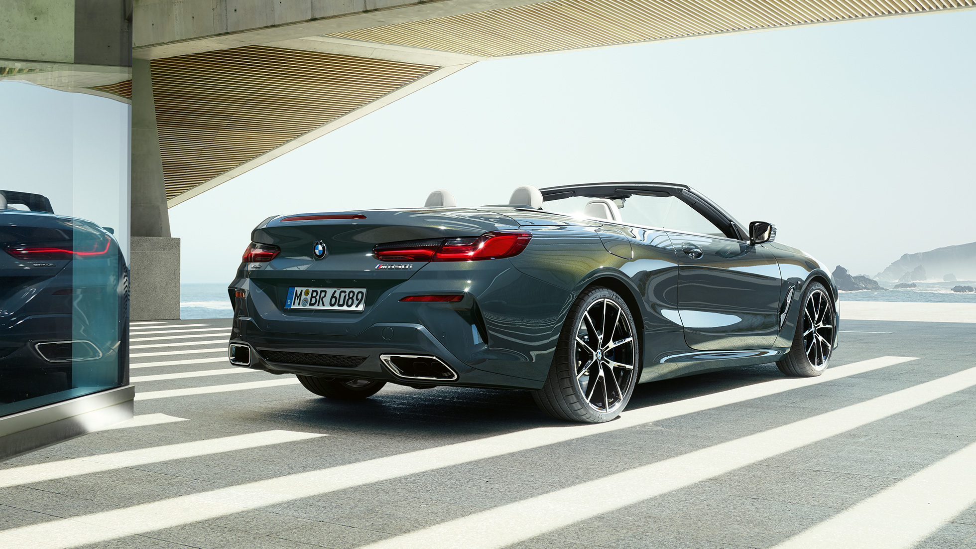 BMW M850i xDrive Cabrio, arkadan görünüm. Açık softtop ile metalik Gri/Dravit BMW M850i xDrive, okyanus manzarası önünde park halinde, arkadan görünüm.