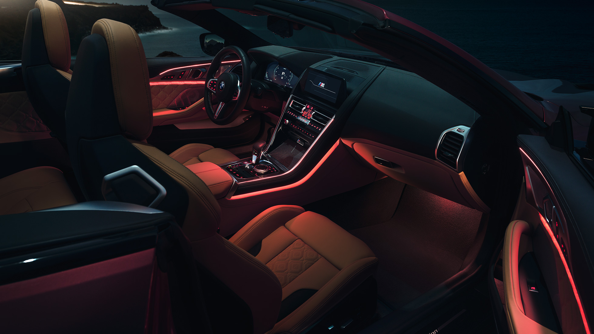 BMW M8 Competition Cabrio, iç tasarım. Gece kırmızı ortam aydınlatmasıyla, açık softtop ile BMW M8 Competition Cabrio’nun iç tasarımı.