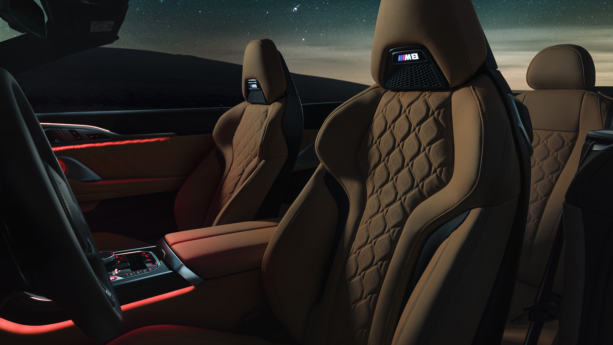 “Merino” deri M Sport koltuklar. “Merino” deri M Sport koltuklar ve kırmızı ortam aydınlatmasıyla yıldızlı gökyüzü altında açık softtop ile BMW M8 Competition Cabrio.