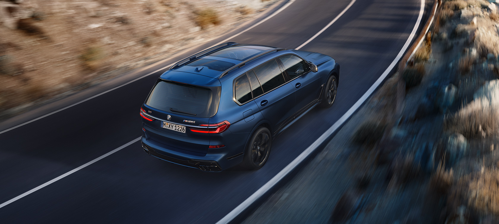 BMW X7 M60i G07 LCI, Metalik Mat Mavi/Marina Bay, yolda sürüş sırasında arka çapraz üstten görünüm