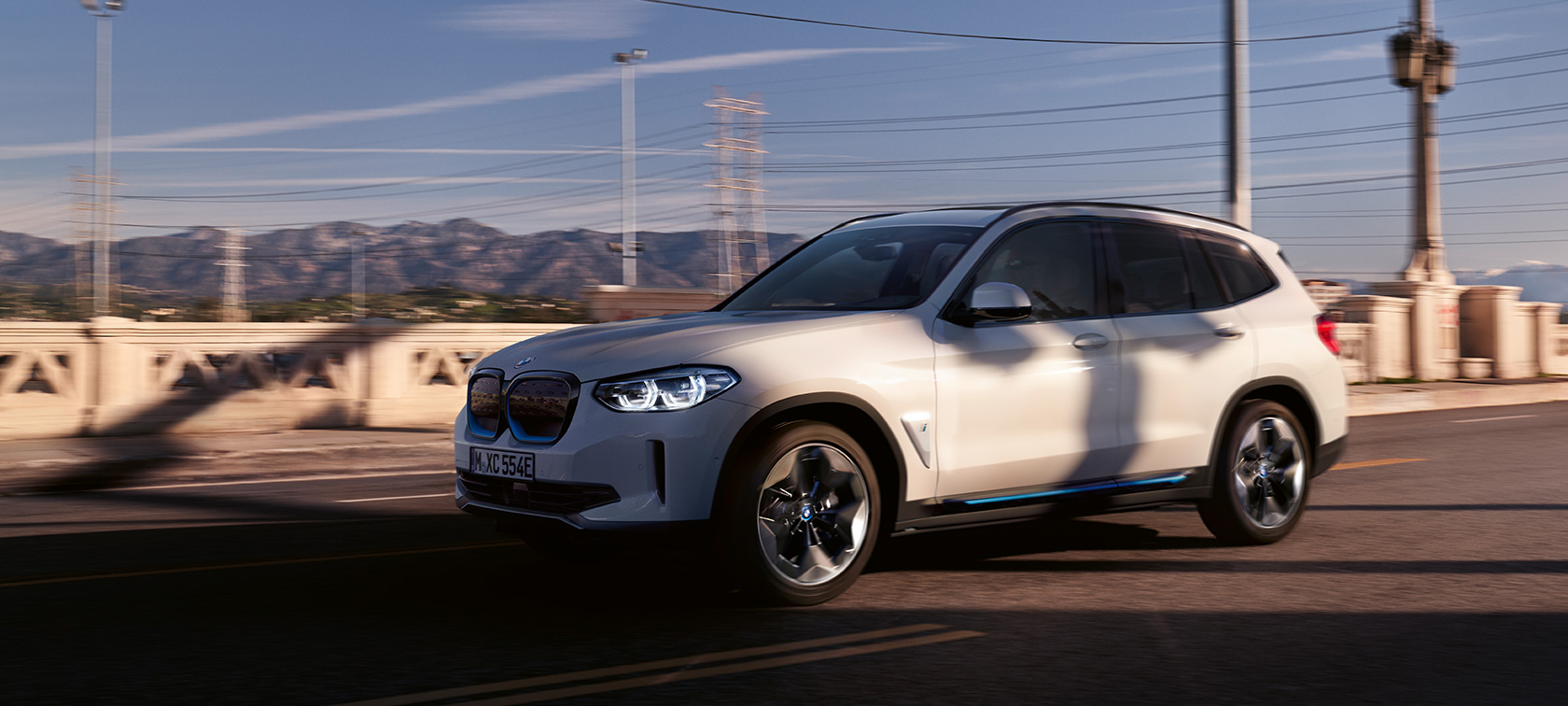 BMW iX3 G08 yolda sürüş sırasında önden görünüm BMW iX3 G08 Metalik Beyaz/Mineral yolda sürüş sırasında önden görünüm