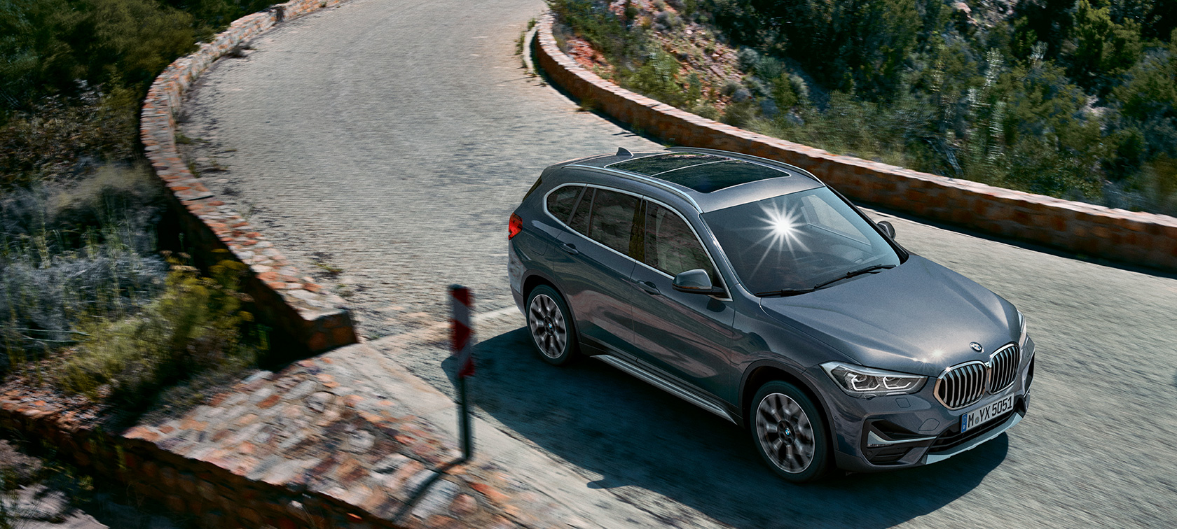 Yeni BMW X1, önden görünüm. Yeni BMW X1, dağ manzarası önünde seyir halinde, önden görünüm.