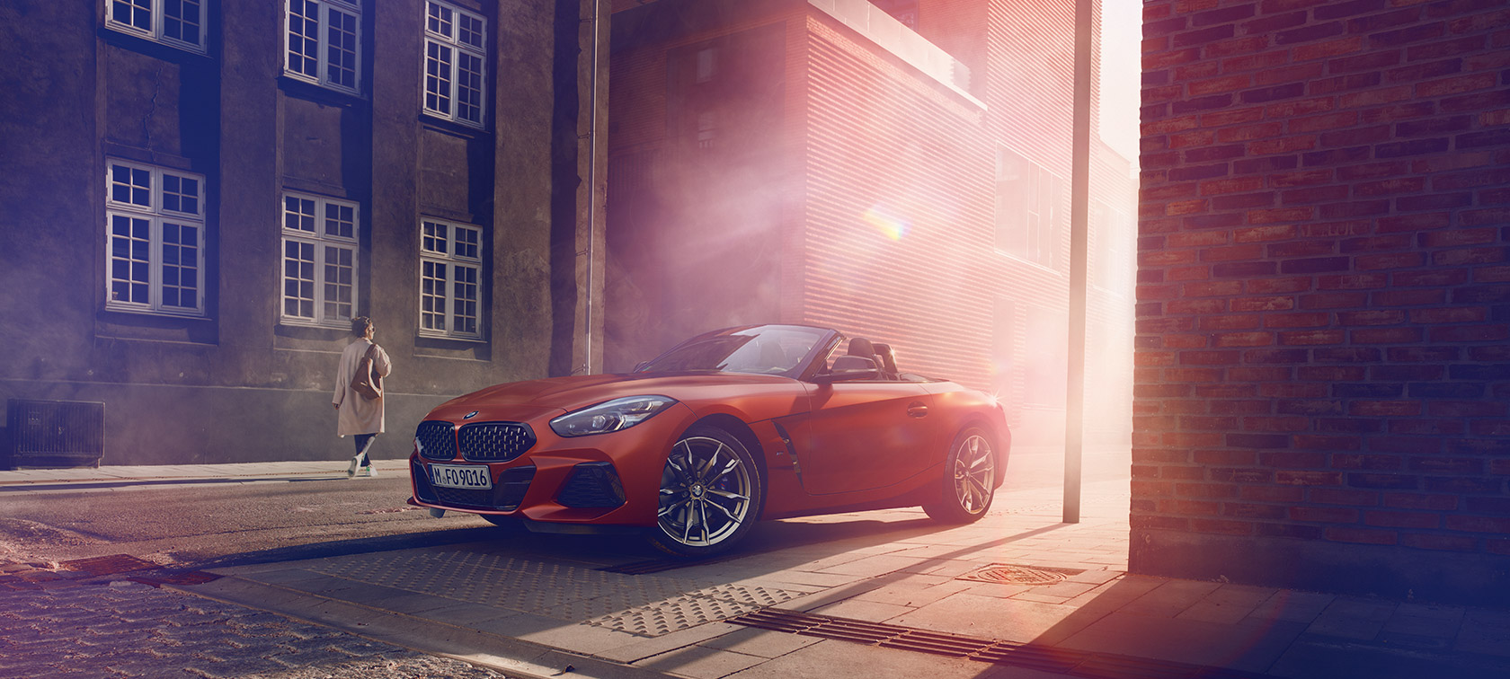 Turuncu renkte Yeni BMW Z4 First Edition Turuncu Yeni BMW Z4 First Edition yarı aydınlık bir sokakta, kadınlarla birlikte evlerin önünde