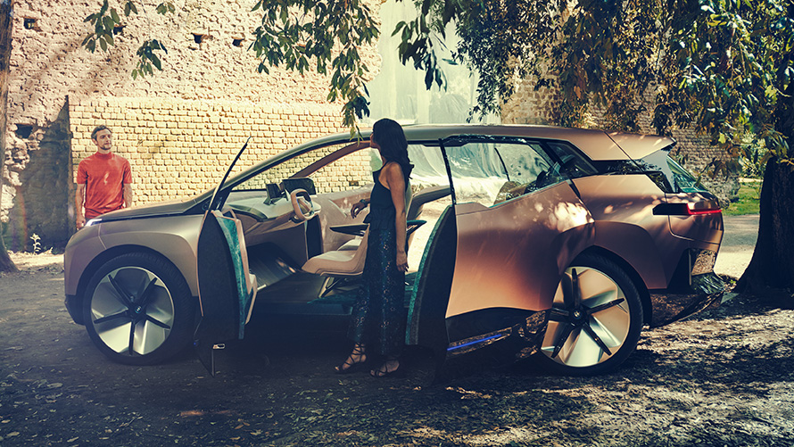 BMW Vision iNEXT’in yandan görünümü Açık kapıda bir kadın ve arka planda bir adam ile BMW Vision iNEXT’in yandan görünümü