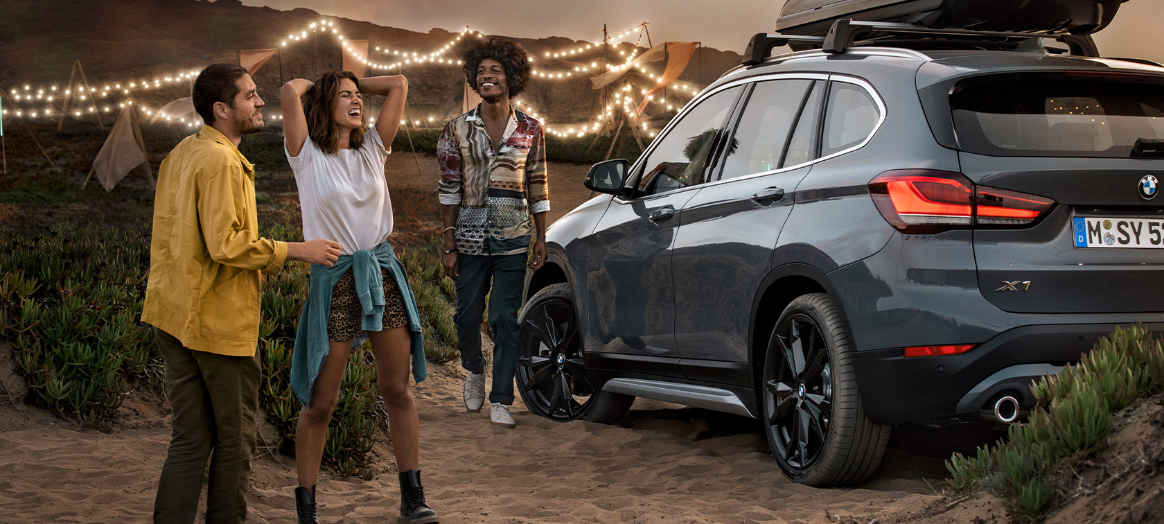 BMW yaz aksesuarları ile donatılmış BMW X1’de mutlu üç arkadaş Plajda BMW yaz aksesuarları ile donatılmış Metalik Gri/Mineral renkte BMW X1’de üç mutlu arkadaş, BMW donanımı