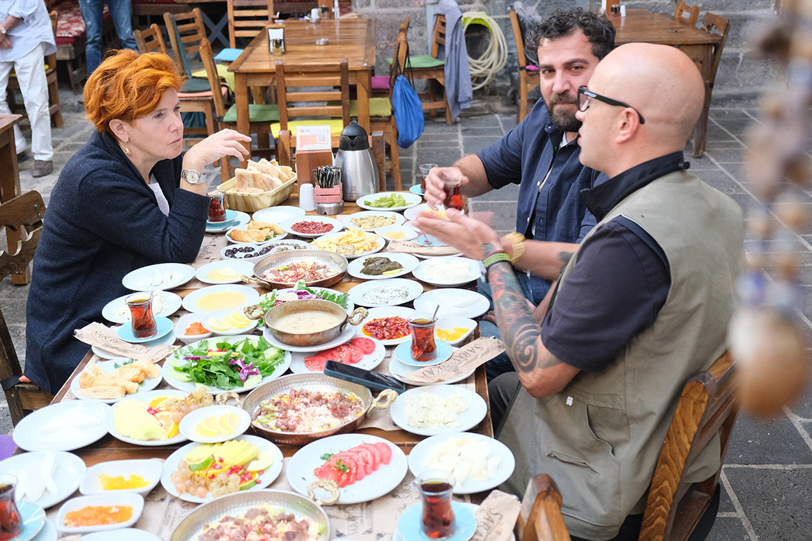 Diyarbakır’ı ziyaret edeceğimiz günü sabırsızlıkla bekliyordum ve sonunda buradayız. Zamanımız oldukça kısıtlı olmasına rağmen olabildiğince etkili kullanmaya çalışacağız. İlk durağımız Palace Gate Cafe & Breakfast’ta Şemsa ve Maksut ile buluşuyoruz. Diyarbakır’ın serpme kahvaltısını henüz denemediyseniz, ilk denemenizi burada yapabilirsiniz. Palace Gate Cafe & Breakfast ayrıldıktan sonra kendimizi Ciğerci Ramazan’da buluyoruz. Kahvaltıda doyasıya yememişiz gibi burada ara sıcaklara adeta saldırıyor, üstüne bir de kebapları mideye indiriyoruz. Buranın kebapları, bu lezzet yolculuğunda yediğim kebaplar arasında ilk beşe girer. Sonrasında ağzımız tatlansın diyerek Kadayıfçı Sıtkı Usta’nın Sur’daki şubesinin yolunu tutuyoruz. Buranın kadayıfları, hele hele fıstıklı kadayıkları yeme de yanında yat tadında. Diyarbakır ile Mardin arasında yer alan tarihî yapı ve askerî yerleşim alanı Zerzevan Kalesi’ne ziyaretimizin ardından Fırın-ci Sur’a geçiyoruz. Aslında pek aç değiliz, bize bir kâse çorba yeter de artar. Fakat masamıza ikramlar geldikçe geliyor, biz de geldikçe yiyoruz. Günü bitirirken, BMWlicious projesi kapsamında çıktığımız lezzet yolculuğunun son durağı burası oluyor. Bu proje sayesinde ülkemizin geleneksel, kültürel ve folklorik değerlerini, zenginliklerini ve en önemlisi lezzetlerini bir kez daha keşfedebildiğim için kendimi çok şanslı hissediyorum. Şemsa, Maksut ve benim rotalarımız ve dolayısıyla keşiflerimiz birbirinden oldukça farklıydı. E, zaten bu farklılık da ülkemizin en güzel yanlarından biri değil mi? Bu projenin gerçekleşmesini sağlayan BMW ailesine ve tüm ekiplere katkı ve desteklerinden dolayı teşekkürlerimi yolluyorum. Başka bir lezzet yolculuğunda görüşmek üzere. Diyarbakır’ı ziyaret edeceğimiz günü sabırsızlıkla bekliyordum ve sonunda buradayız. Zamanımız oldukça kısıtlı olmasına rağmen olabildiğince etkili kullanmaya çalışacağız. İlk durağımız Palace Gate Cafe & Breakfast’ta Şemsa ve Maksut ile buluşuyoruz. Diyarbakır’ın serpme kahvaltısını henüz denemediyseniz, ilk denemenizi burada yapabilirsiniz. Palace Gate Cafe & Breakfast ayrıldıktan sonra kendimizi Ciğerci Ramazan’da buluyoruz. Kahvaltıda doyasıya yememişiz gibi burada ara sıcaklara adeta saldırıyor, üstüne bir de kebapları mideye indiriyoruz. Buranın kebapları, bu lezzet yolculuğunda yediğim kebaplar arasında ilk beşe girer. Sonrasında ağzımız tatlansın diyerek Kadayıfçı Sıtkı Usta’nın Sur’daki şubesinin yolunu tutuyoruz. Buranın kadayıfları, hele hele fıstıklı kadayıkları yeme de yanında yat tadında. Diyarbakır ile Mardin arasında yer alan tarihî yapı ve askerî yerleşim alanı Zerzevan Kalesi’ne ziyaretimizin ardından Fırın-ci Sur’a geçiyoruz. Aslında pek aç değiliz, bize bir kâse çorba yeter de artar. Fakat masamıza ikramlar geldikçe geliyor, biz de geldikçe yiyoruz. Günü bitirirken, BMWlicious projesi kapsamında çıktığımız lezzet yolculuğunun son durağı burası oluyor. Bu proje sayesinde ülkemizin geleneksel, kültürel ve folklorik değerlerini, zenginliklerini ve en önemlisi lezzetlerini bir kez daha keşfedebildiğim için kendimi çok şanslı hissediyorum. Şemsa, Maksut ve benim rotalarımız ve dolayısıyla keşiflerimiz birbirinden oldukça farklıydı. E, zaten bu farklılık da ülkemizin en güzel yanlarından biri değil mi? Bu projenin gerçekleşmesini sağlayan BMW ailesine ve tüm ekiplere katkı ve desteklerinden dolayı teşekkürlerimi yolluyorum. Başka bir lezzet yolculuğunda görüşmek üzere.