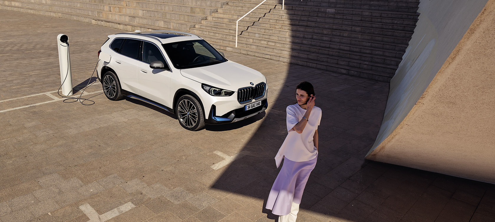 BMW iX1 U11 BEV, Metalik Beyaz/Mineral, Virajlı dağ yolunda sürüş sırasında ön çaprazdan görünüm