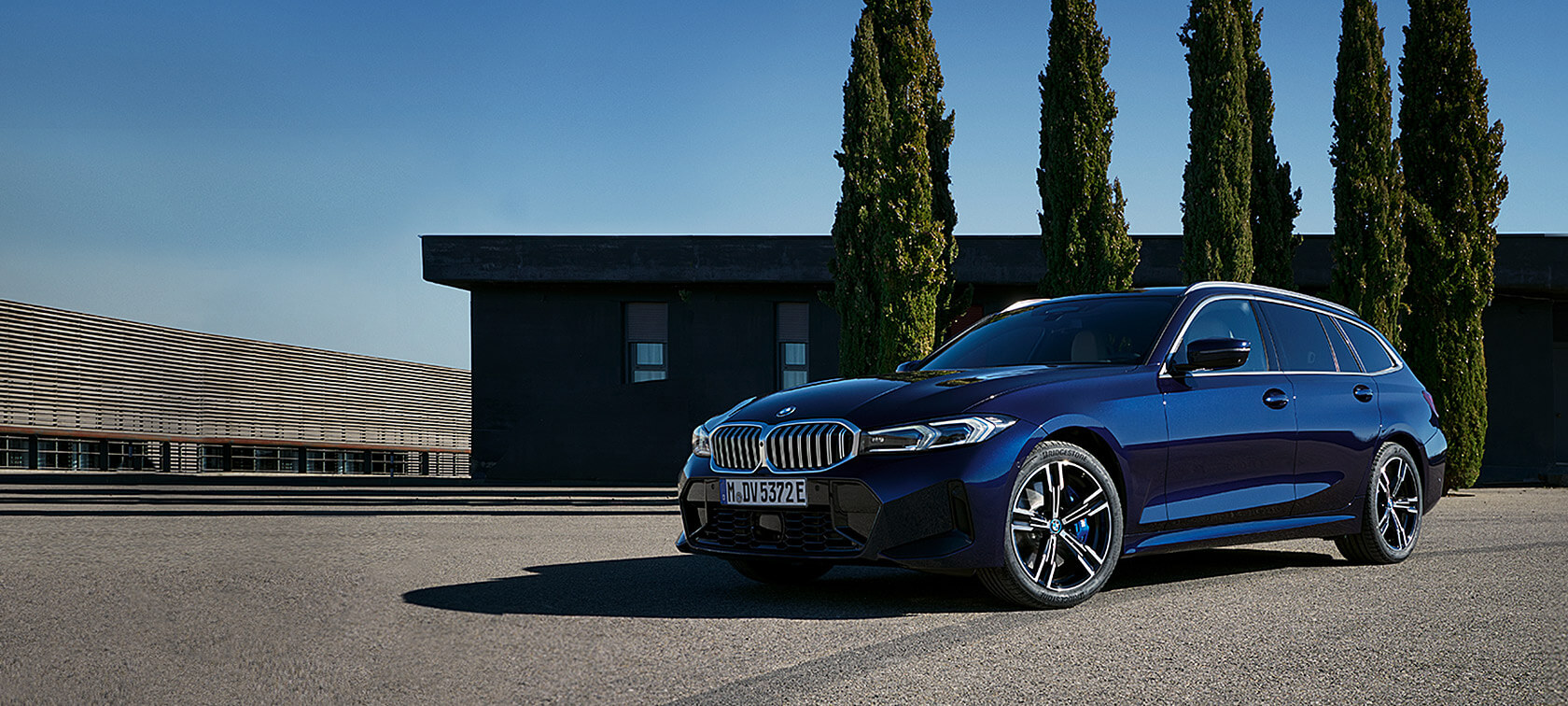BMW 3 Serisi Touring LCI G21, Metalik Mavi/Tanzanite Blue II, ağaçların önünde hareketsiz halde ön çaprazdan görünüm