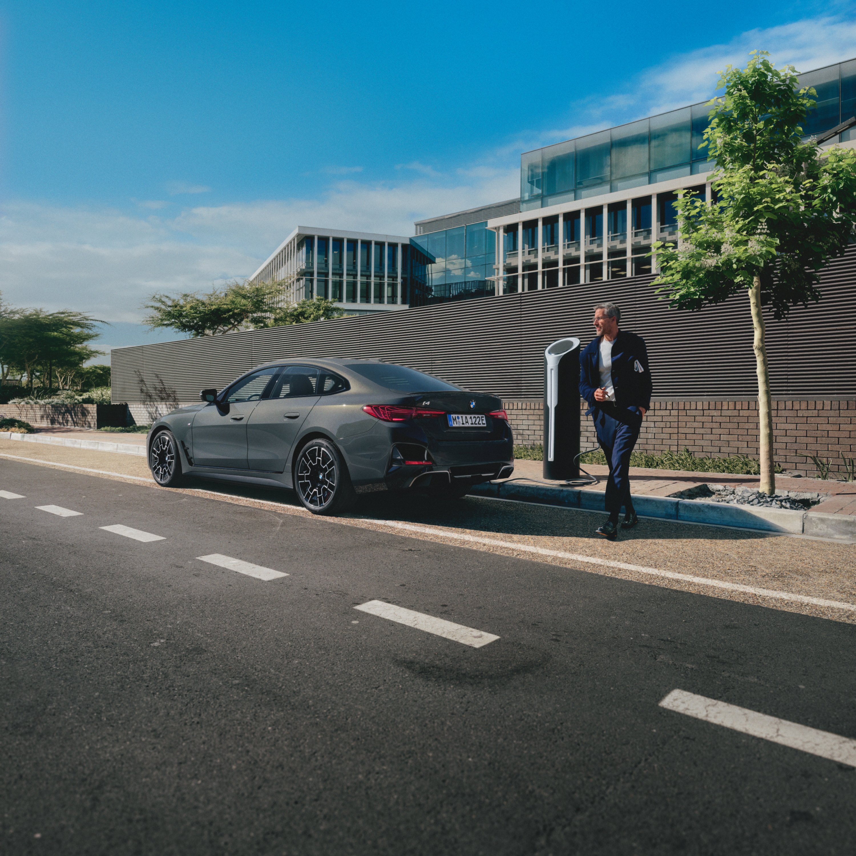 Bir kişi yol kenarında şarj halinde bir BMW'nin arkasında duruyor