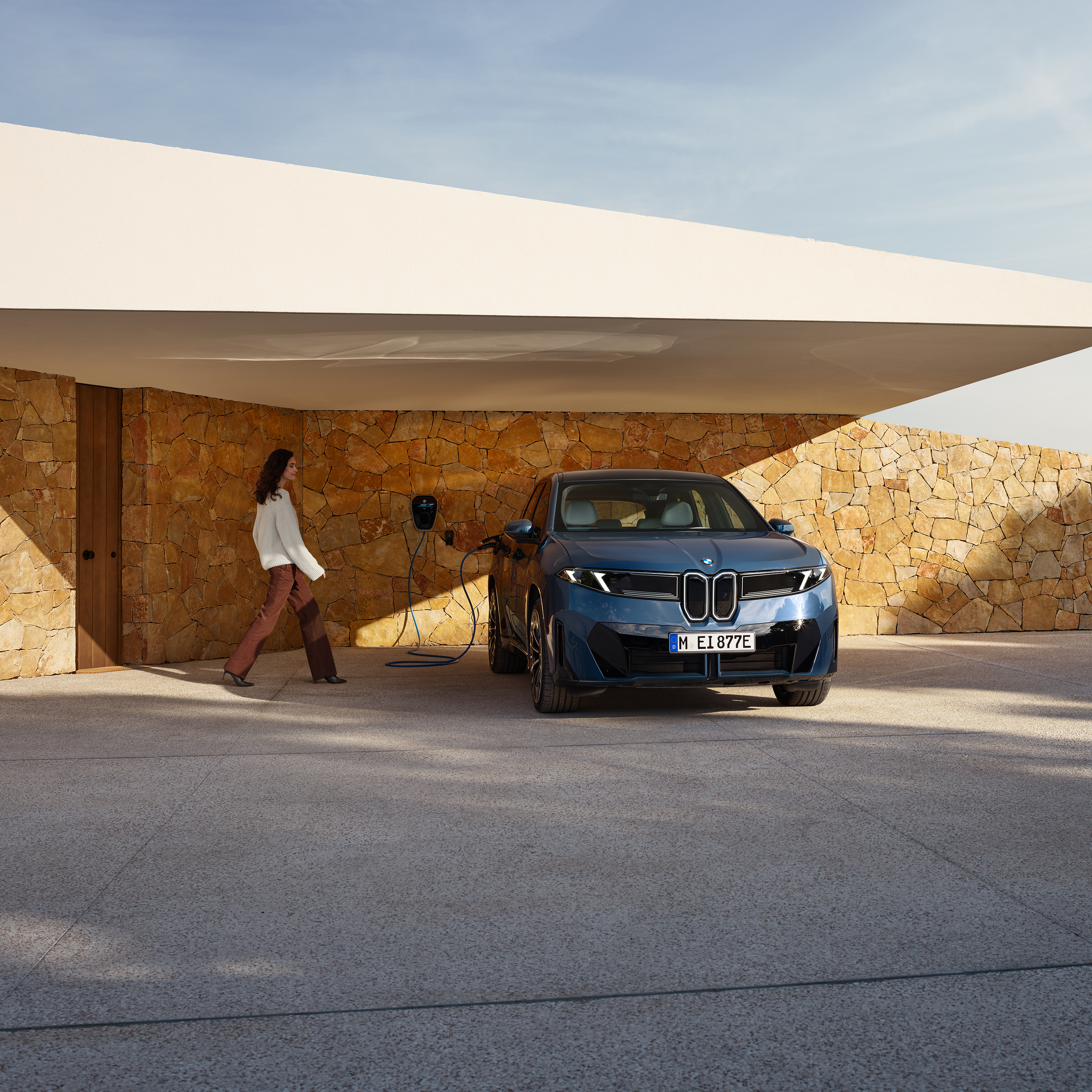 Bir kadın wallbox’a takılı bir BMW iX3'e doğru yürüyor